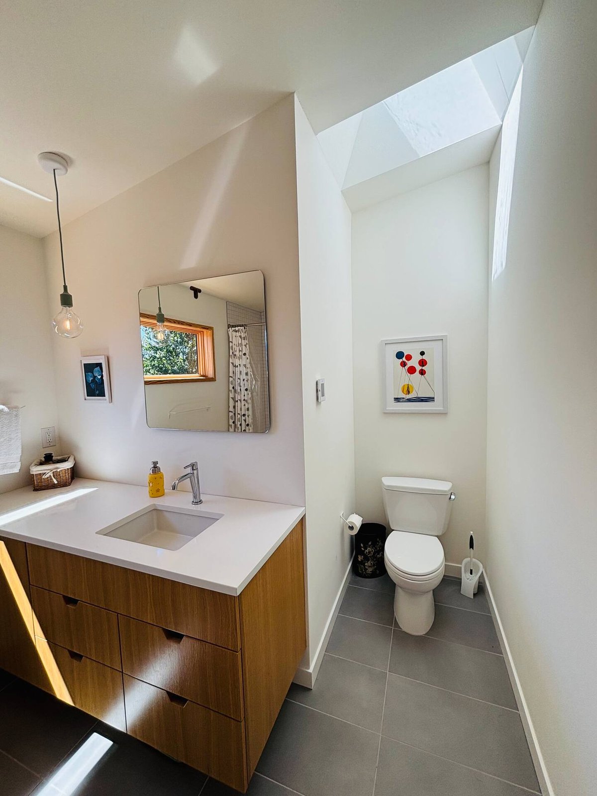 Second bathroom with walnut vanity, pendant light, skylight, and modern art