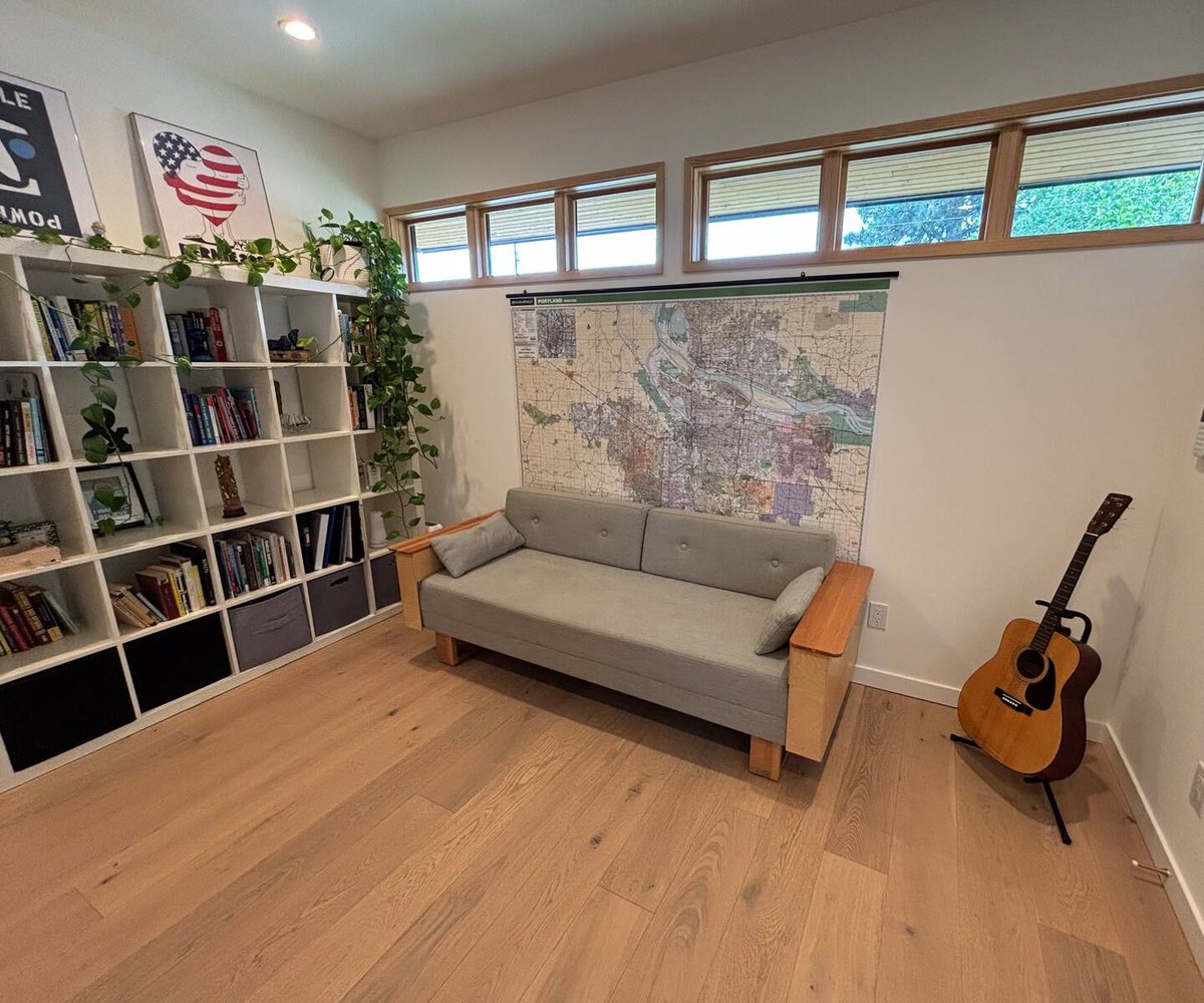 Den with sleeper sofa, Portland map, bookshelf with trailing plants, and guitar