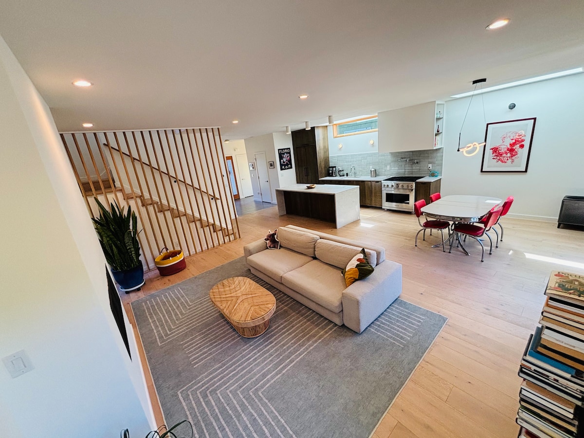 Open-concept Scandinavian modern living room with wood slatted staircase, sectional sofa, and kitchen in Portland Oregon vacation home