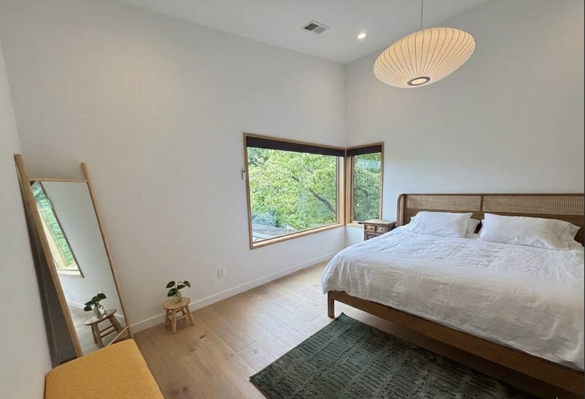 Primary bedroom with king bed, pendant light, green rug, and treetop views