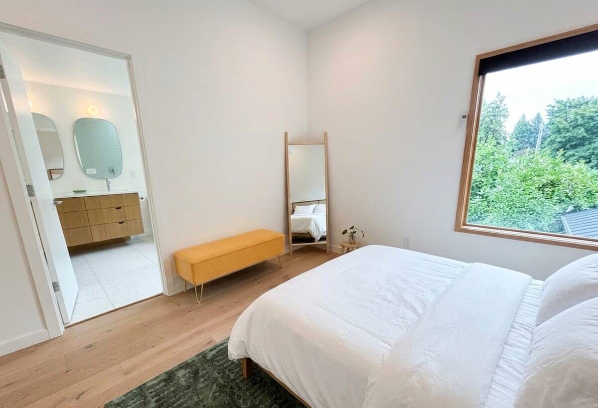 Primary bedroom with en-suite bathroom, yellow bench, standing mirror, and garden views