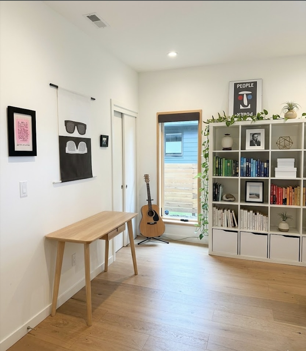 Home office with wood bench desk, guitar, bookshelf, and wall art