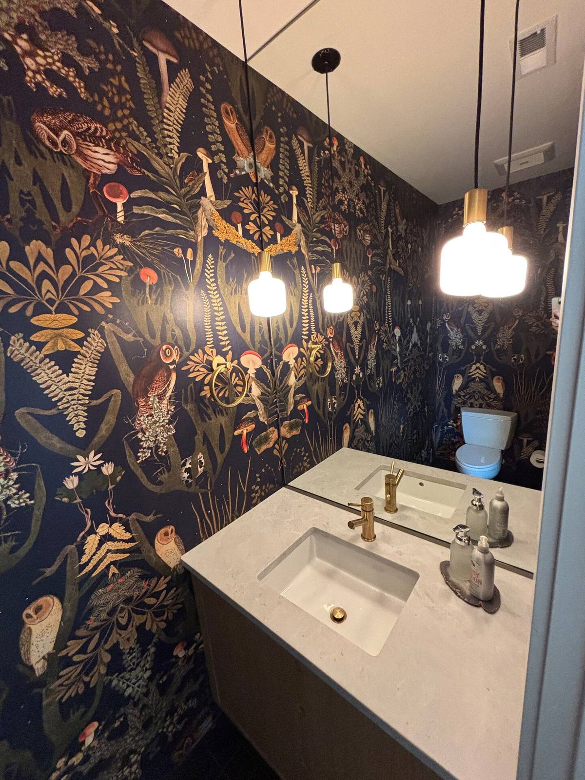 Powder room with forest mushroom wallpaper, brass pendant lights, and brass fixtures