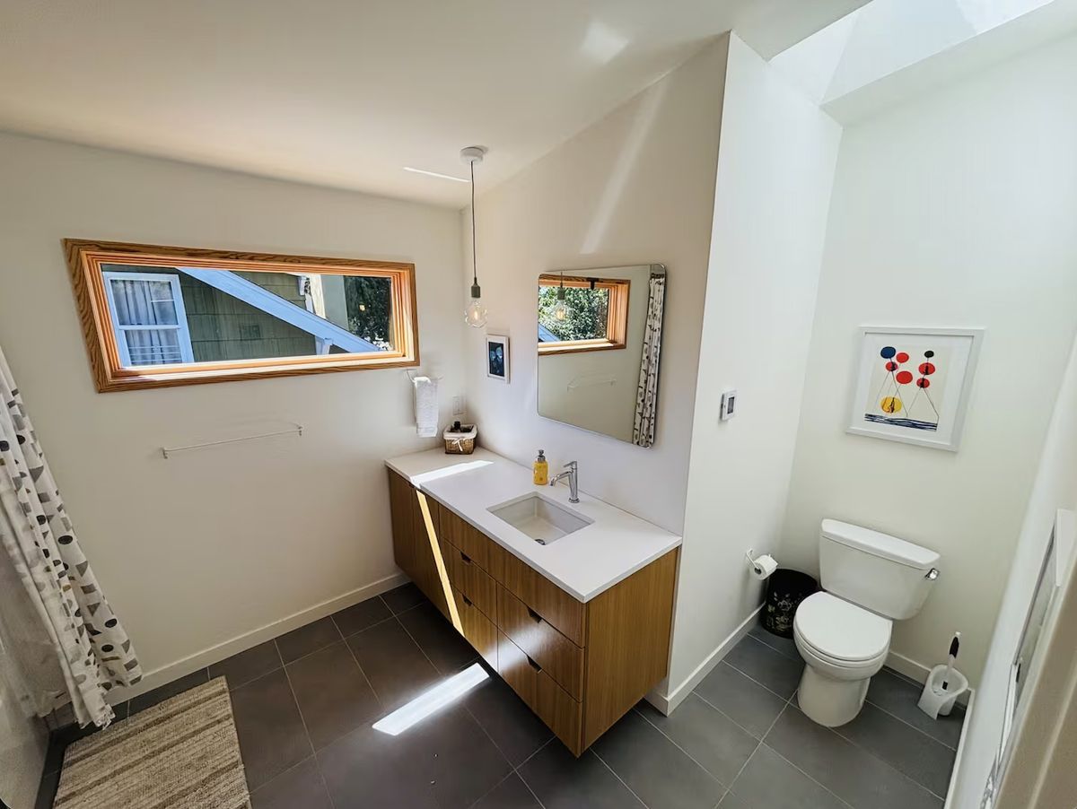 Second bathroom with walnut vanity, pendant light, art, and grey tile floor
