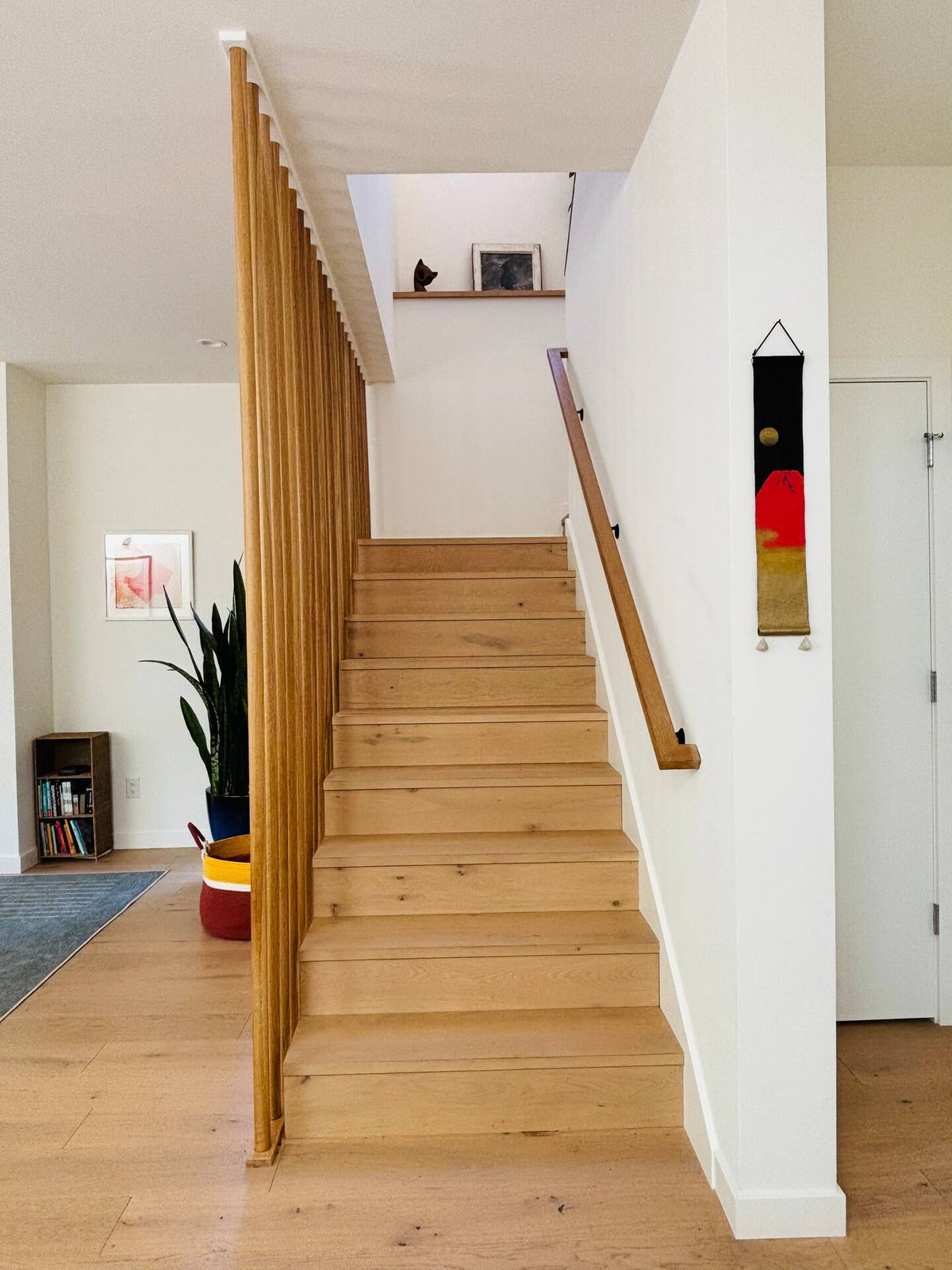 Wood slatted staircase with oak treads, handrail, art, and plants